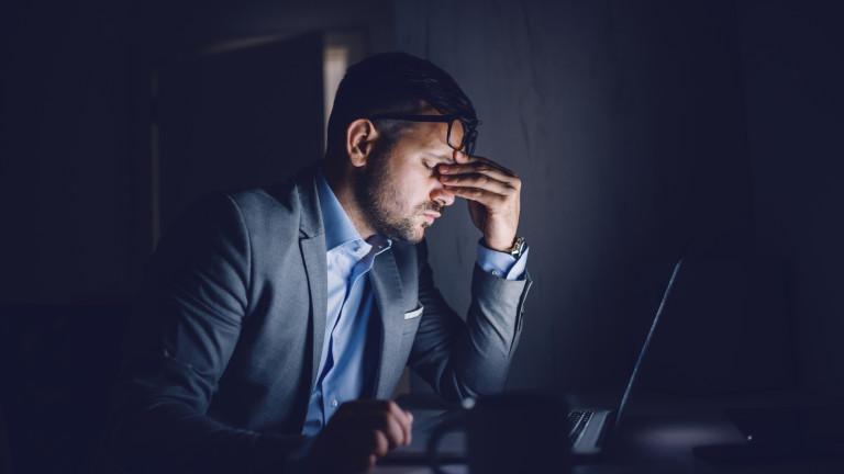 Tired hardworking handsome Caucasian businessman sitting in office late at night and rubbing eyes. In front of his is laptop. Overworking concept.