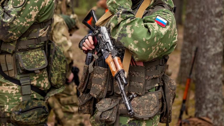 Close up hands russian soldier man dressed military camouflage uniform holds weapon in woodland at soldiers background. Male border guard in country border holding machine gun on war. Copy text space