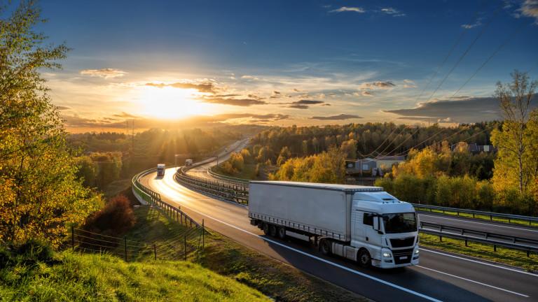 White trucks driving on the highway winding through forested landscape in autumn colors at sunset